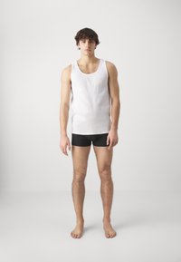 Hvit bomullstopp og svarte boxershorts. Toppen har en vid halslinning; shortsene sitter tett med en jevn tekstur.