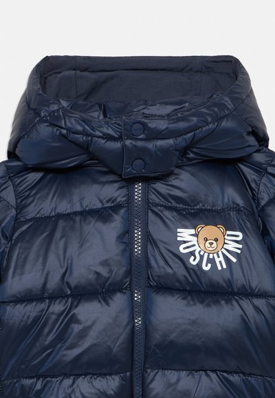 Mornarska pufasta jakna z visokim ovratnikom in gumbnim zapiranjem. Na sprednji strani je bear logo in ime blagovne znamke v beli barvi. Gladka, sijoča tekstura.