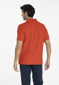 Polo shirt rouge, à manches courtes, en mélange de coton, col classique, fentes latérales ; porté avec un pantalon marine, vue de dos.