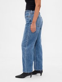 Jeans de denim azul de cintura alta con un diseño de pierna ancha, que presentan un estilo clásico de cinco bolsillos y un acabado sin costura, combinados con botas negras de punta.