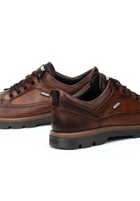 Zapatos de cuero marrón con un acabado texturizado, con cordones negros, punta redonda y una suela de goma duradera. Los detalles incluyen costuras decorativas.