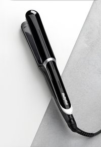 Fer à lisser noir avec un design élégant, des accents argentés et des bords arrondis. Dispose d'une poignée texturée et d'un cordon d'alimentation en spirale.