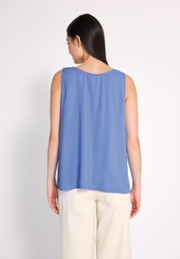 Top blu senza maniche con una texture liscia, scollatura rotonda e vestibilità rilassata, abbinato a pantaloni a gamba larga color avorio.