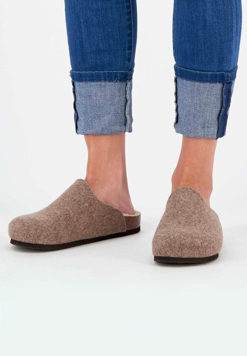 Braune Filzclogs mit einer glatten, abgerundeten Zehe und offenem Rücken. Die Sohle ist dunkel mit einer dezenten Textur und wird mit hochgekrempelten Jeans kombiniert.