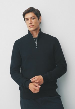 Schwarzer Pullover mit hohem Kragen und Reißverschlussdetails. Gerippte Bündchen und Saum, aus einem strukturierten Strickstoff gefertigt. Slim-fit-Design.