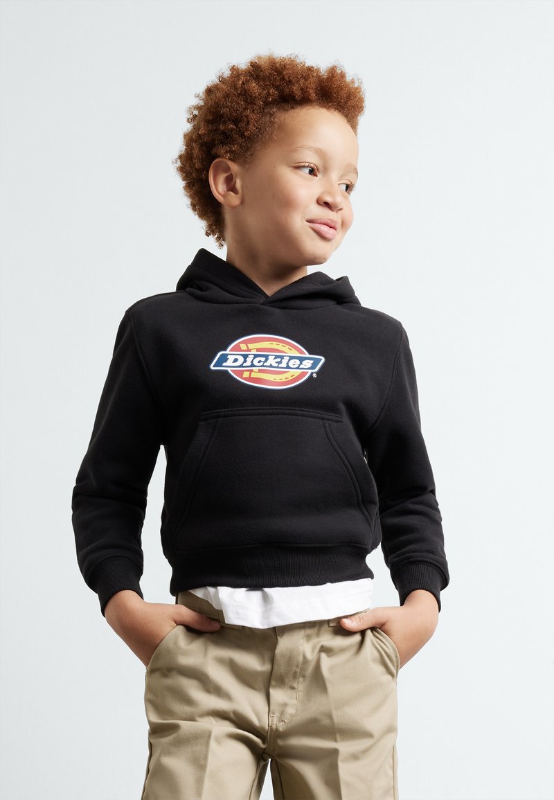 Svart hoodie med en framficka i kangaroo-stil, prydd med en flerfärgad "Dickies"-logotyp. Kombinationen med khaki-byxor och en vit skjorta under.
