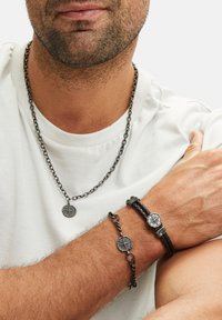 Zwarte metalen ketting met hanger, geweven zwart leren armband en bijpassende ketting, allemaal met decoratieve kompasmotieven.