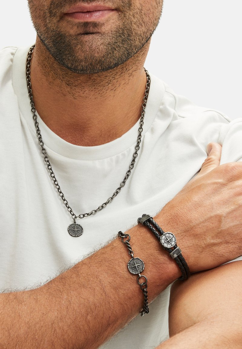 Zwarte metalen ketting met hanger, geweven zwart leren armband en bijpassende ketting, allemaal met decoratieve kompasmotieven.