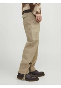 Beige cargo bukser med flere lommer, lige ben-design, robust stof og kontrastsyninger. Båret med mørkebrune støvler.