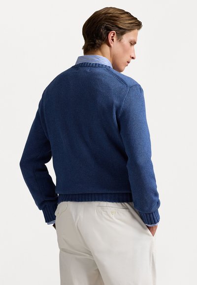 Blue knit sweater with a ribbed hem and cuffs, featuring a classic design and textured fabric. Worn over a collared shirt.