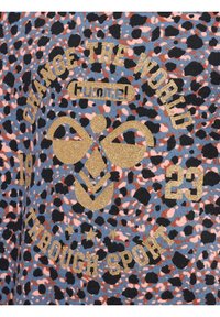 T-shirt med en blå och rosa leopardmönster, med guldglittertext och symboler, inklusive "FÖRÄNDRA VÄRLDEN" och "GENOM SPORT."