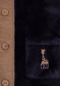 Tessuto in corduroy beige e velluto blu navy con una tasca che presenta un design di una giraffa dorata e bottoni in legno marrone. Texture morbida e materiali a contrasto.