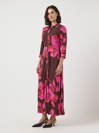Maxikjol i brun tyg med stora rosa blommönster, knapplist framtill, krage och trekvartslånga ärmar.