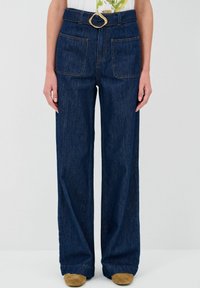 Jeans in denim a gamba larga di colore blu scuro con cuciture visibili, due tasche frontali e una fibbia della cintura tonalità oro.