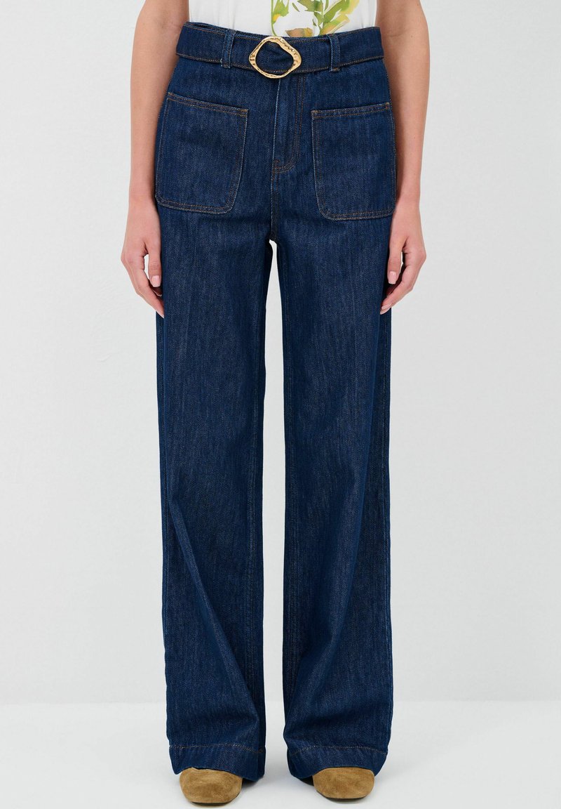 Jeans in denim a gamba larga di colore blu scuro con cuciture visibili, due tasche frontali e una fibbia della cintura tonalità oro.