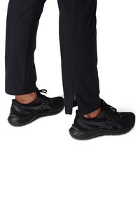 Czarne buty sportowe z oddychającą siateczkową cholewką, amortyzowaną podeszwą i teksturowanymi detalami; zestawione z czarnymi spodniami z bocznym zamkiem błyskawicznym.