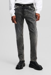 Gray denim jogger pants with a black drawstring waistband, featuring front pockets and a tapered leg design. Worn with black chunky boots.