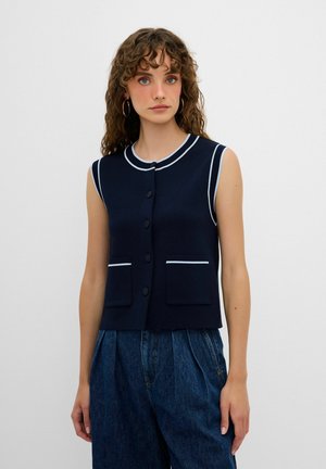 Marineblauwe mouwloze vest met witte accenten, voorzien van een ronde kraag, vijf knopen aan de voorkant en twee opgestikte zakken. Gladde stoftextuur.