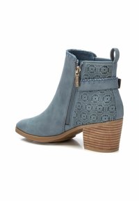 Bottine en cuir bleu avec des accents perforés, fermeture éclair sur le côté et un talon empilé marron. Texture lisse avec des détails de couture décorative.