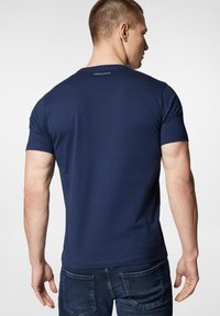 Granatowa bawełniana koszulka z krótkim rękawem, okrągłym dekoltem i małym logo na plecach. Gładka tekstura i dopasowany krój.