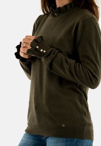 Maglione lavorato a maglia verde oliva con un motivo a pois texturizzato, scollatura arricciata e dettagli con bottoni sulle maniche. Design aderente con orlo a coste.