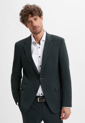 Dark green blazer made of textured fabric with a slim fit, notched lapels, and two front pockets, paired with a white shirt and black belt.