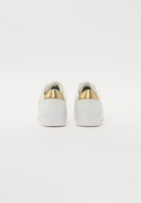 Baskets blanches à finition lisse, avec un talon arrière doré texturé et une semelle en caoutchouc blanche. Logo embossé à l'arrière.