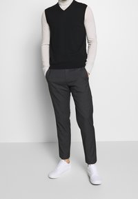 Black knitted vest over a light turtleneck, paired with dark gray tapered trousers and white sneakers. Simple, modern design and clean lines.