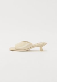 Mules beiges à enfiler avec un dessus en polyuréthane lisse et brillant, bout ouvert et un petit talon carré.
