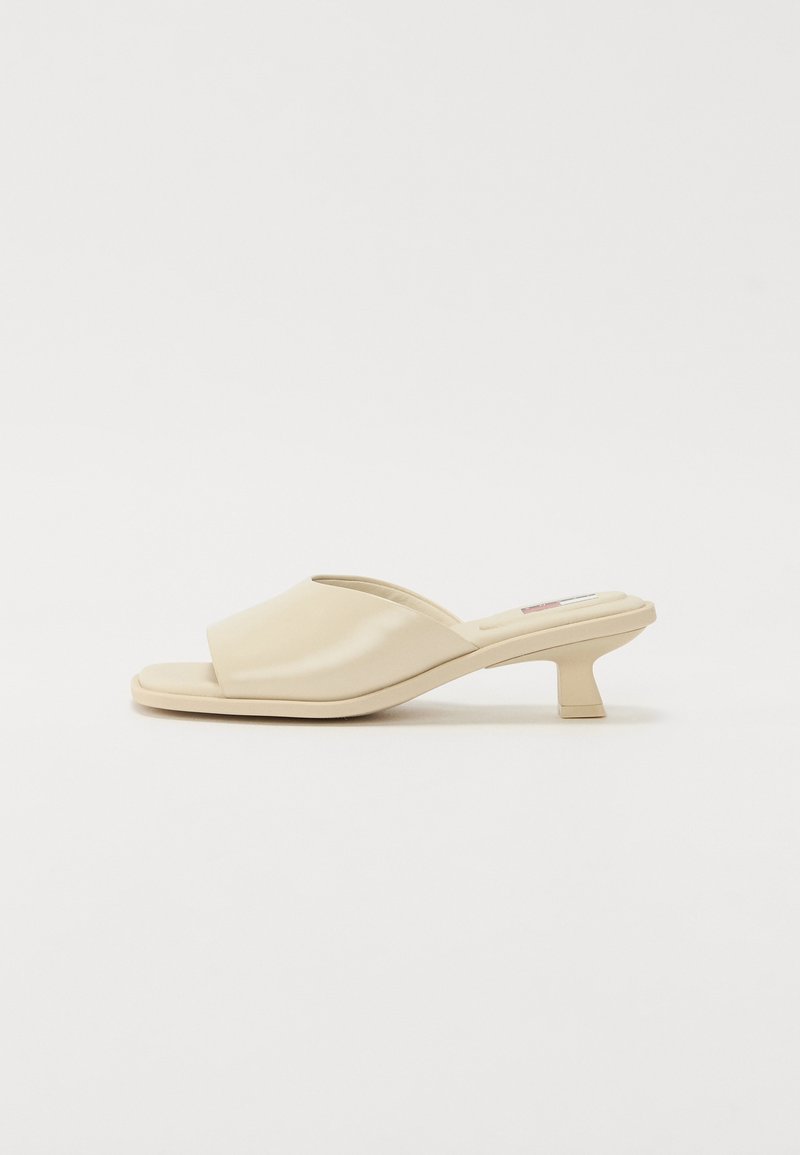 Mules beiges à enfiler avec un dessus en polyuréthane lisse et brillant, bout ouvert et un petit talon carré.