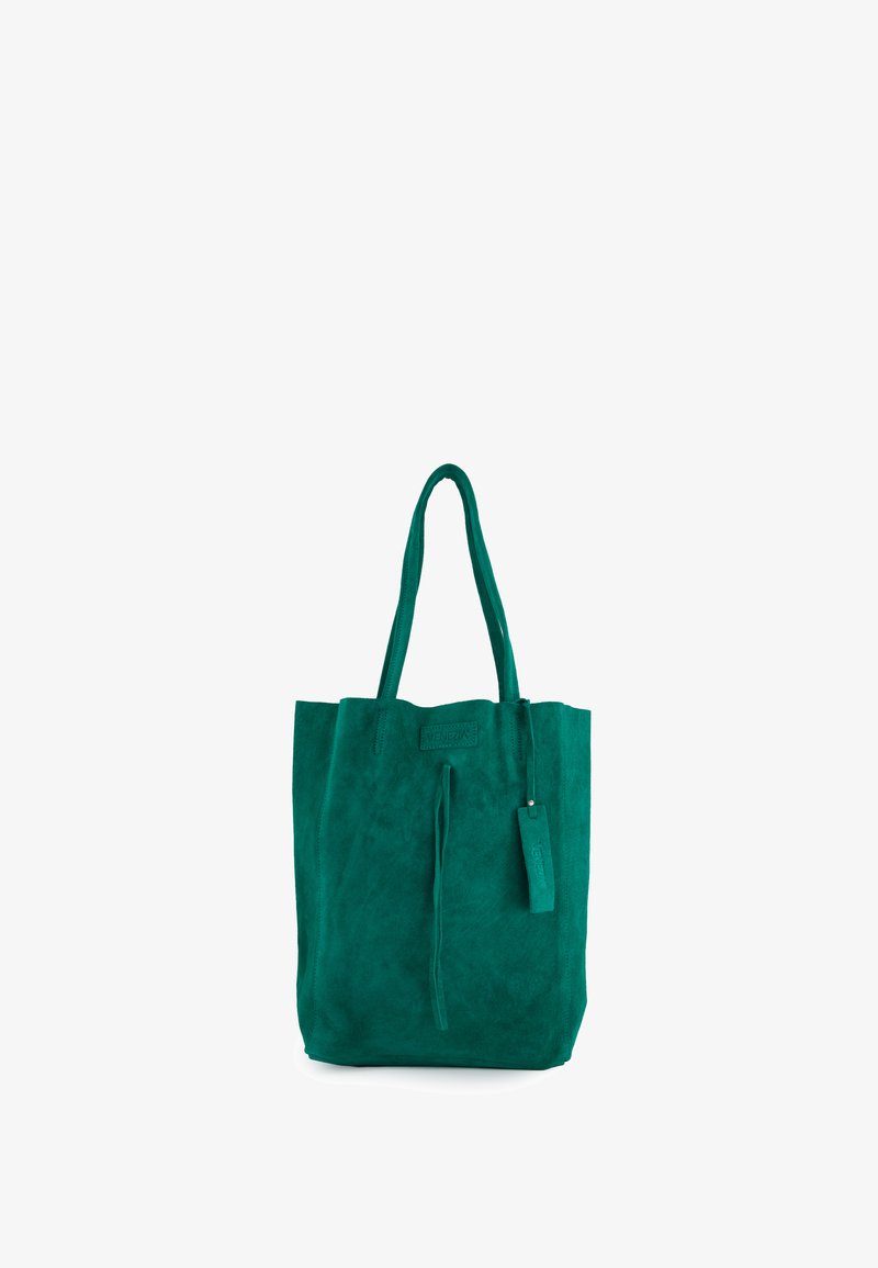 Groene suède shopper met lange hengsels en een hangend leren label, rechtopstaand op een witte achtergrond.