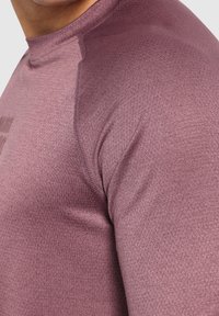 Dlouhý rukáv sportovní tričko z texturované, tmavě fialové látky s přiléhavým střihem a vysokým límcem, s kontrastními švy.