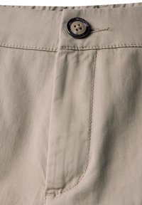 Beige bomullsbyxor med knappstängning, en stor frontficka och synliga sömnadsdetaljer längs sömmarna.