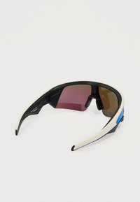 Gafas de sol con montura en blanco y negro, diseño curvado, lentes con degradado rosa y marrón, y detalle azul en el lateral. Agarre texturizado en las patillas interiores.