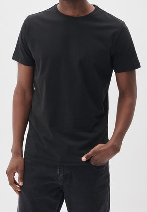 Zwarte T-shirt met korte mouwen van katoen met een ronde hals. Eenvoudig ontwerp, gladde textuur, aansluitende pasvorm, gecombineerd met donkere jeans.