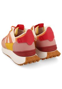 Des sneakers combinant des matériaux rouges, roses, jaunes et crème avec un revêtement arrière texturé et une semelle en caoutchouc proéminente.
