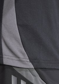 Maglietta sportiva nera con un pannello testurizzato grigio di lato, realizzata in tessuto liscio e con accenti geometrici sottili vicino all'orlo.