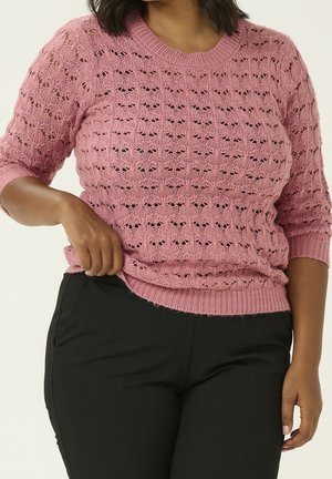 Knit pink sweater with short sleeves, featuring an openwork pattern and ribbed neckline and hem. Paired with black pants.