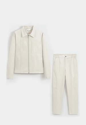 Veste beige clair avec fermeture éclair et poche poitrine, associée à un pantalon cargo assorti avec taille élastique et poches latérales.