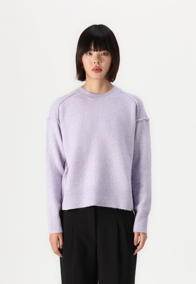 Pull en lilas tricoté avec un ourlet et des poignets côtes, présentant une coupe décontractée et des manches raglan. Texture douce et apparence légère.