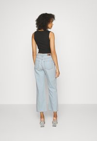 Top preto, jeans de perna larga azul claro com bolsos traseiros, cintado na cintura, combinado com sandálias de salto alto de xadrez.