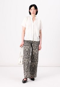 Witte overhemd met textuurdetails, gecombineerd met zwart-beige wijde zebrapatroon broeken. Zwarte loafers en een witte handtas.