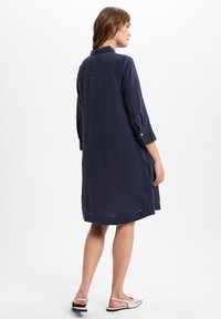 Marineblaue Leinenkleid mit entspanntem Schnitt, Dreiviertelärmeln und einer Knopfdetails an den Manschetten. Mittel lang, mit weichem Textur und Kragen.