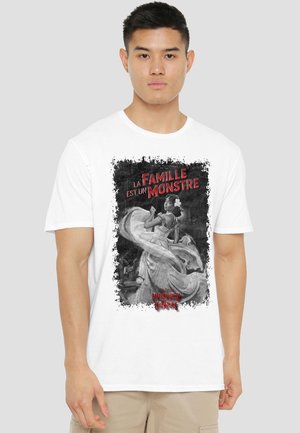 Young man wearing white T-shirt with black-and-white vintage-style woman in flowing dress and red French text "La Famille est un Monstre."