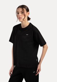 Svart bomull t-shirt med rund halsringning och korta ärmar. Har en liten logotyp på bröstet och en etikett vid sidan av sömmen.