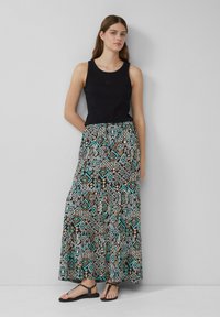 Schwarzes, geripptes Trägershirt kombiniert mit einem langen, gemusterten Maxikleid, das geometrische Designs in Türkis, Braun und Weiß aufweist. Flache schwarze Sandalen.