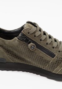 Sneaker in suede verde oliva con superficie texture, dettagli in zip nera e lacci abbinati, caratterizzati da una robusta suola in gomma nera.