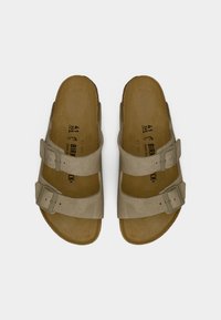 Μπεζ σουέντ σανδάλια με δύο ρυθμιζόμενα λουριά και μεταλλικές αγκράφες. Διαθέτουν ανατομική σόλα και υφή υλικού με φυσική όψη.