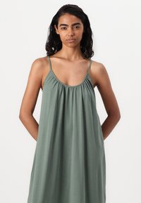 Sleeveless green dress made from soft fabric, featuring a scooped neckline and gathered waist, flowing silhouette down to the mid-calf.