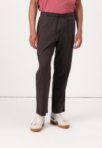 Mørkegrå bomullsbukser med elastisk midjebånd og snor, med en smal passform og sidelommer. Brukt med beige sneakers.